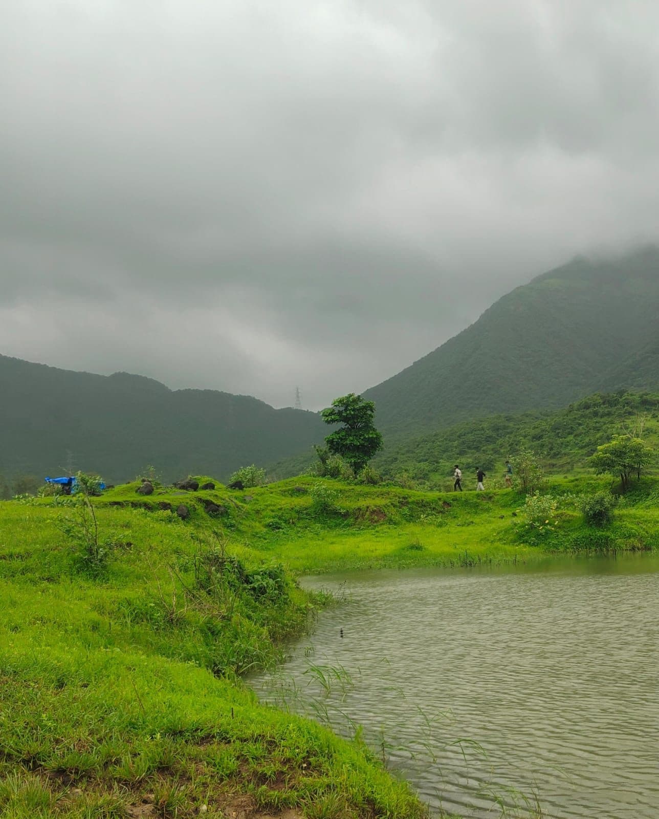 A still lake in the foreground with a green ridgeline and low cloud behind it.